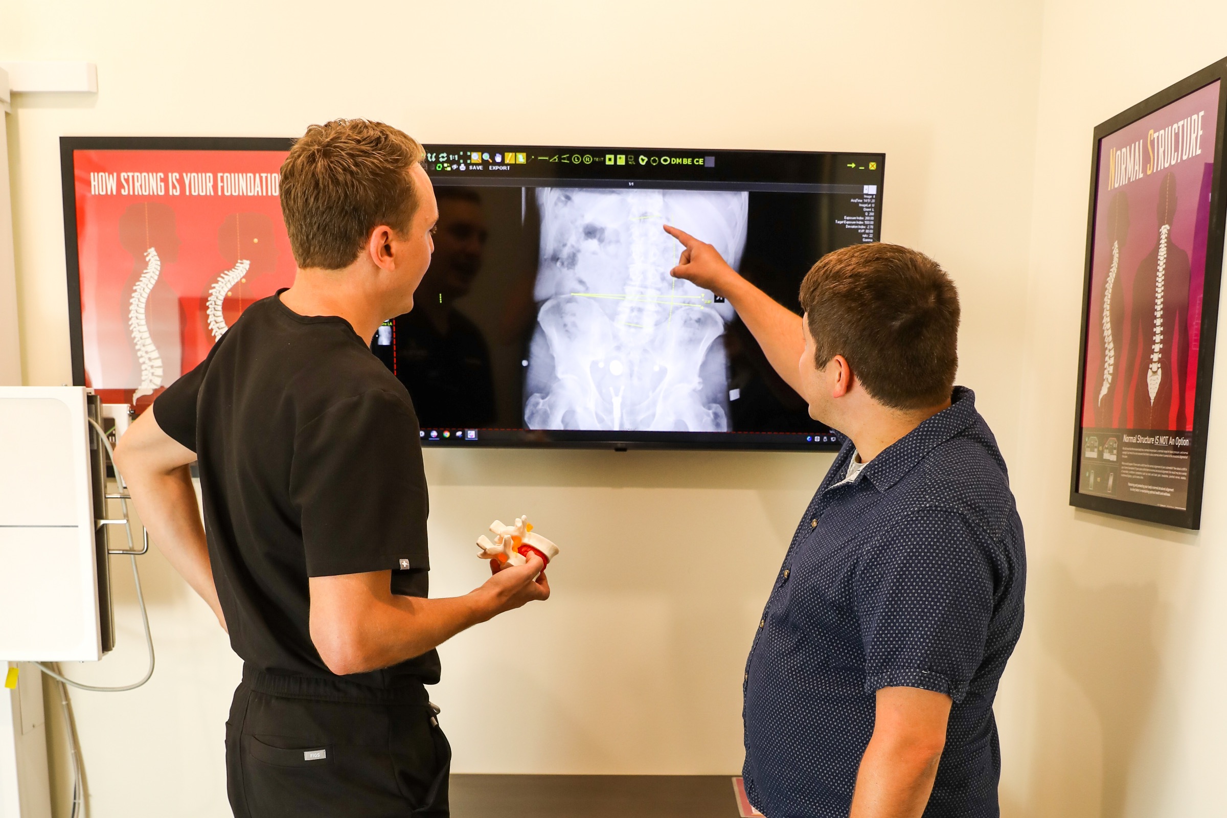 Dr. Lucas Emmerich holding a spine model while a patient points at his X-ray at Central Health in Altoona, WI